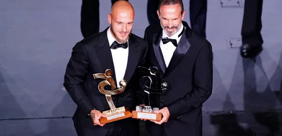 Dos hombres en trajes sosteniendo premios en escenario
