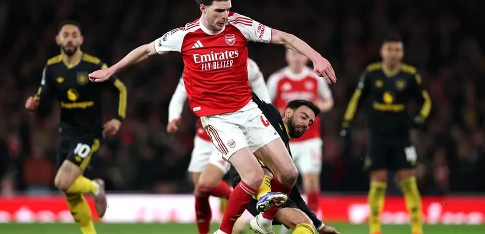 Jugador del Arsenal driblando mientras es tackleado