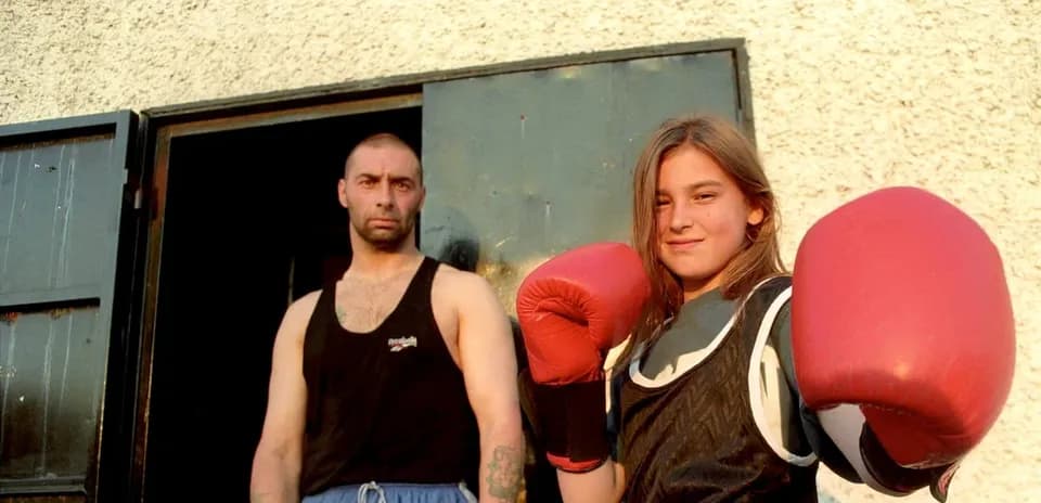Niña con guantes de boxeo y entrenador en puerta