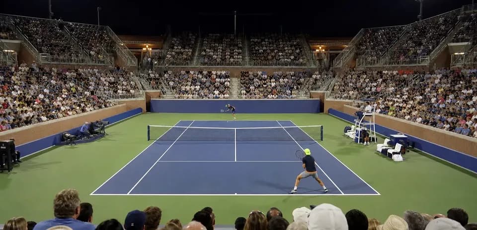 Partido de tenis en cancha iluminada con público