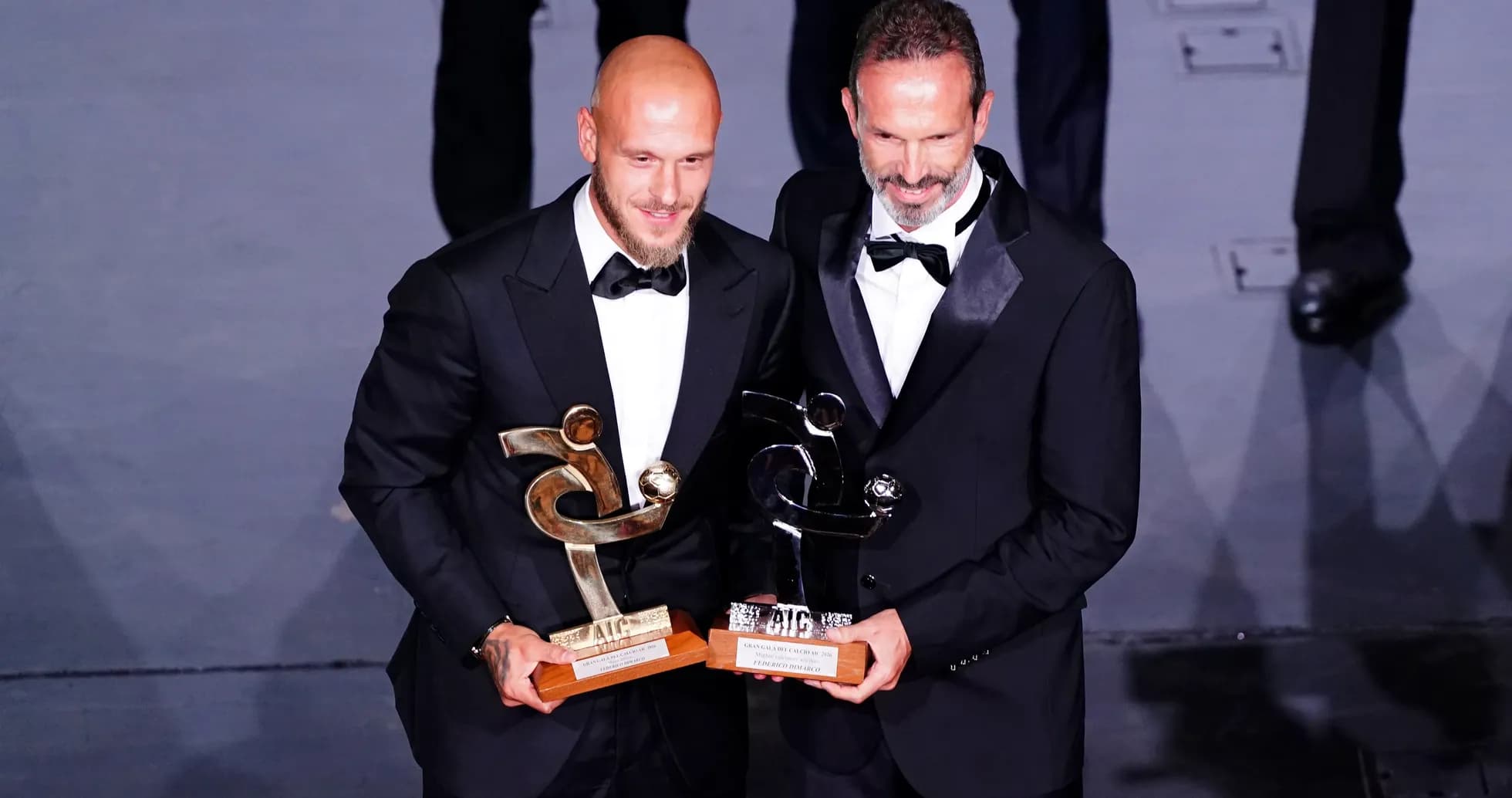 Dos hombres en trajes sosteniendo premios en escenario Dos hombres en trajes sosteniendo premios en escenario