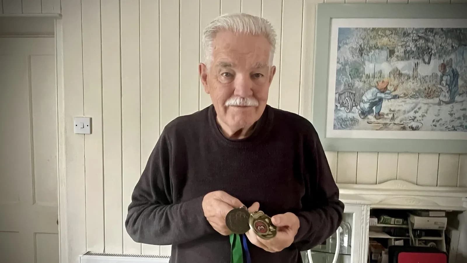 Hombre mayor sosteniendo medallas en casa Hombre mayor sosteniendo medallas en casa